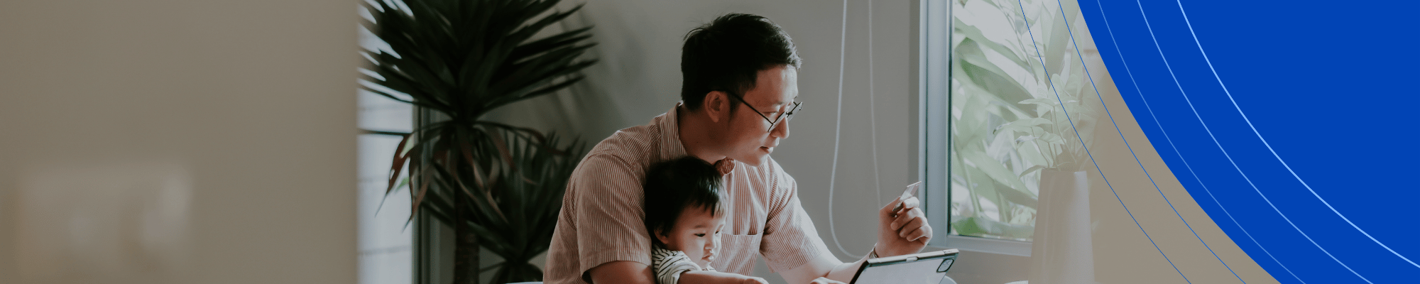 man with dark hair holding a baby while seated at a table