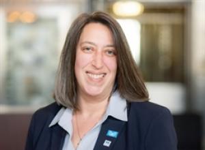 Woman with brown hair smiling wearing navy blue business suit